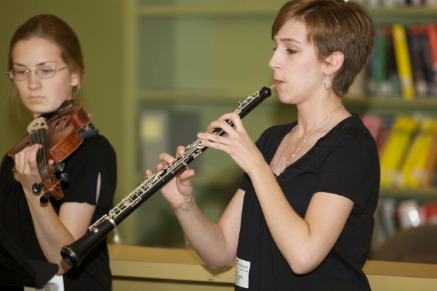 Zwei Frauen mit Klarinette und Geige, mit unscharfen Bücherregalen und einer Wand im Hintergrund.