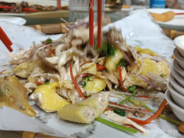 A dining table with plates of food, bowls of sauce, chopsticks, glasses, bottles, and other items in a restaurant or bar setting, with a person visible in the background.