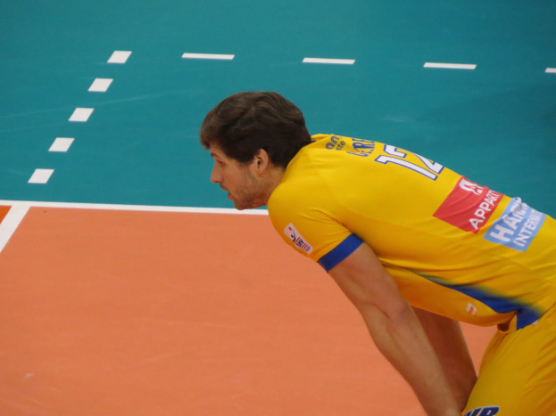 Eine professionelle Volleyballspielerin in einem gelben T-Shirt mit der Aufschrift "Volleyball" steht selbstbewusst auf einem Court und ist bereit, den Ball zu servieren.
