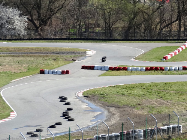 Rennstrecke mit zahlreichen Reifen an ihren Rändern, umgeben von Gras und Maschendrahtzaun, mit Bäumen im Hintergrund.