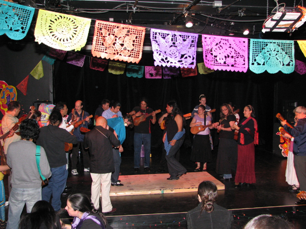 Menschen mit Musikinstrumenten auf einer Bühne mit Dekorationen und Lichtern darüber.