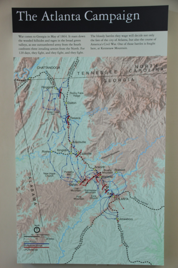 Ein Plakat an einer Wand, das eine detaillierte Karte der Atlanta-Kampagne zeigt, einschließlich Straßen, Städten und Sehenswürdigkeiten, mit begleitendem Text über das Datum, die Uhrzeit und den Ort der Kampagne.