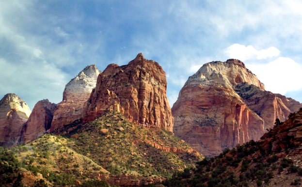 Zion-Nationalpark in Utah mit majestätischen Bergen, grünen Bäumen, steinigem Gelände und einem Himmel voller weißer Wolken.