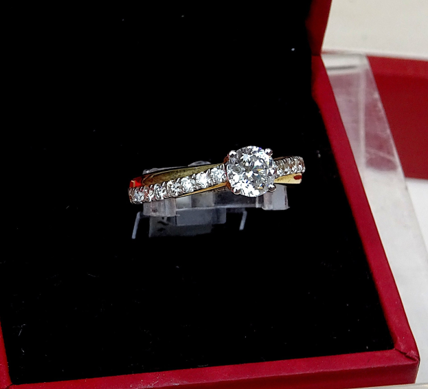 A deep red box containing a diamond engagement ring with a halo of smaller diamonds, placed on a table.