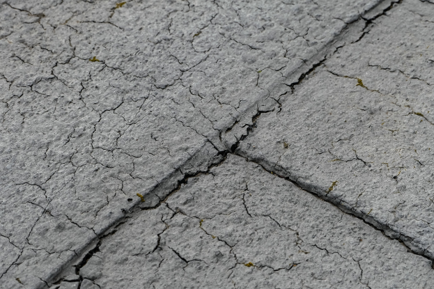 Nahaufnahme einer gebrochenen und verwitterten Straßenoberfläche mit tiefen, breiten Rissen und einer rauen, unebenen Textur.