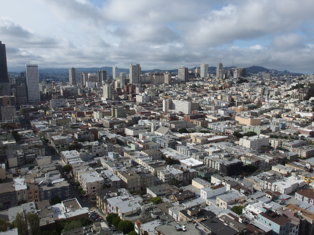 Eine dicht bebaute Stadtlandschaft mit zahlreichen Häusern, Gebäuden und hohen Türmen, mit minimaler Grünfläche und einem sichtbaren Himmel im Hintergrund.