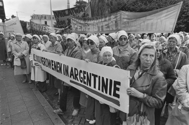 Eine Gruppe von Frauen hält ein Banner mit der Aufschrift "Argentinischer Frauenmarsch in Argentinien" in einer Außenumgebung mit Bäumen, Gebäuden, einer Ampel und einem bewölkten Himmel.