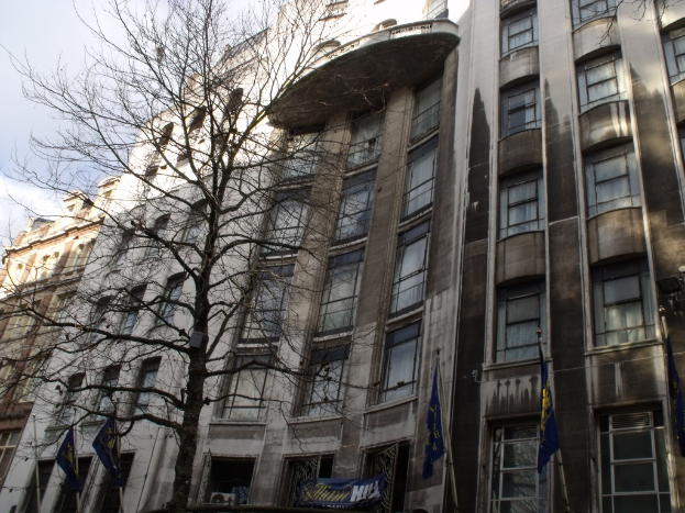 Gebäude mit Fenstern, einem Banner und Fahnen an Stangen unten und einem Baum mit Zweigen.
