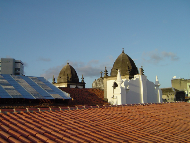 Eine Stadtansicht mit Gebäuden im Vordergrund, einem blauen Himmel im Hintergrund und Solarpanelen auf einem Dach.