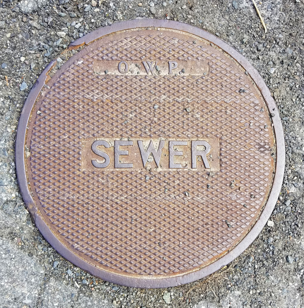 Ein runder Metallschachdeckel auf dem Boden mit dem Wort "Kanal" darauf geschrieben.