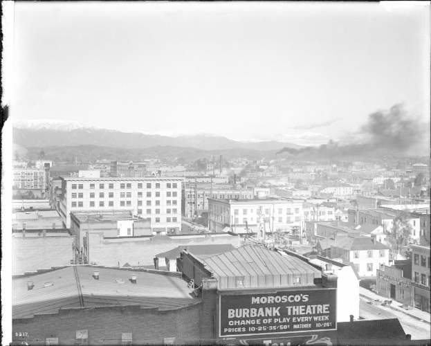 Ein Schwarz-Weiß-Bild einer Fabrik mit Rauch, der aus ihrem Schornstein quillt, umgeben von Gebäuden.