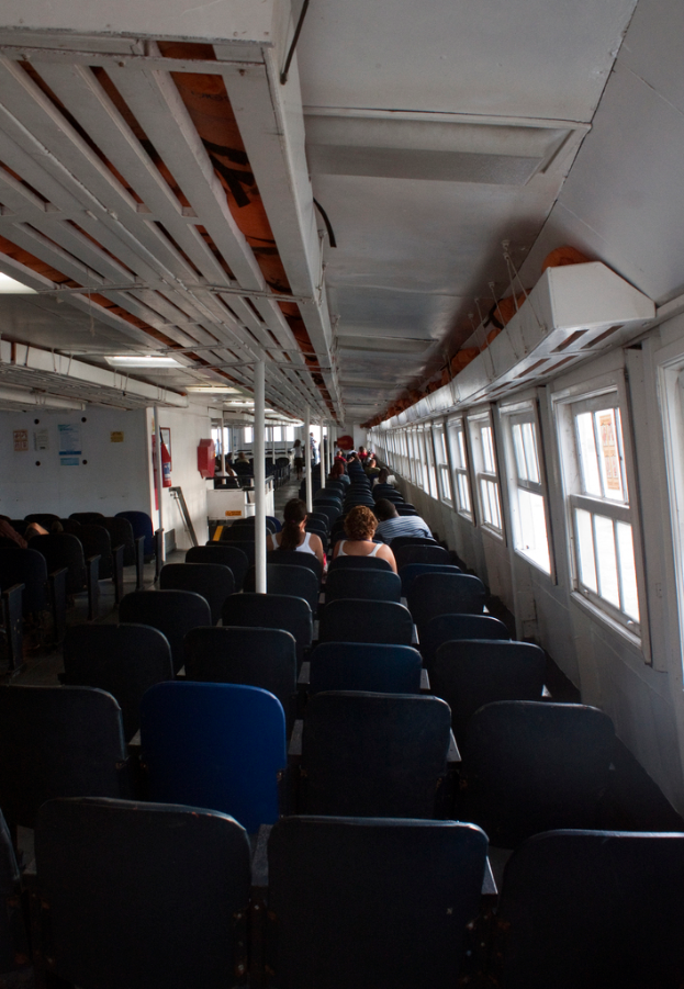 Mehrere Stühle sind in einem Raum angeordnet, in dem drei Personen darauf sitzen, ein Pfahl davor, ein Notfallzylinder, Papiere an der Wand und ein Fenster auf der rechten Seite.