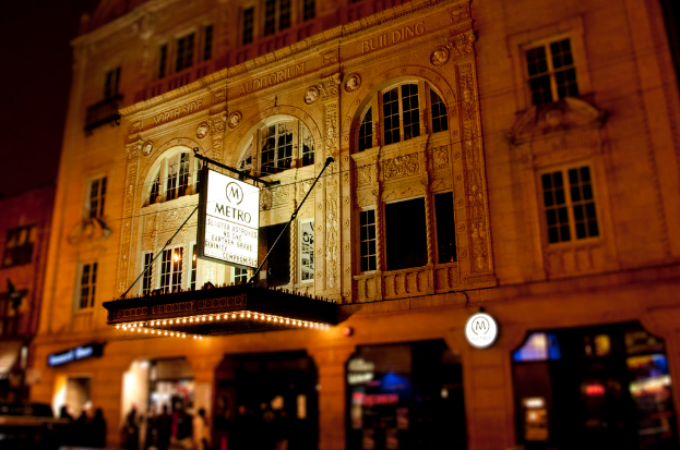 Ein gelbes Gebaeude mit Geschaeften unten und einem weissen Schild mit der Aufschrift "Metro" davor.