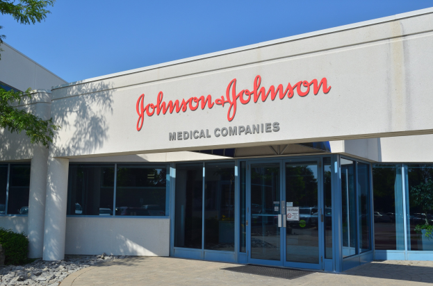Das Johnson & Johnson Medical Companies-Gebäude mit Glaswänden und -türen, Text an der Wand, Steinen, Pflanzen und einem Baum auf der linken Seite, unter einem klaren blauen Himmel.