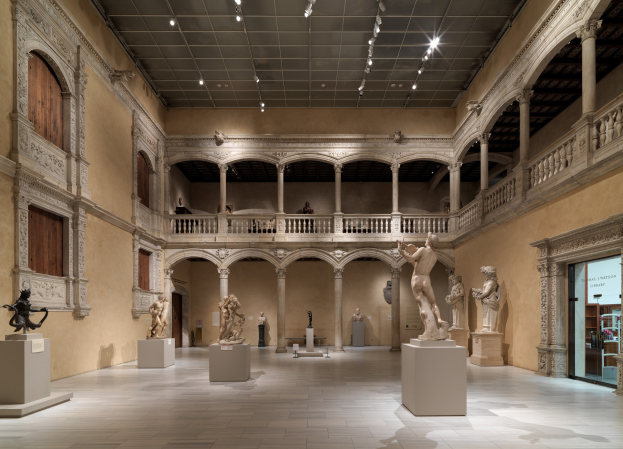 Großer Raum mit zahlreichen Statuen und Skulpturen auf Sockeln, architektonischen Elementen wie Wänden, Säulen und Geländern, Deckenleuchten und einigen Besuchern, ähnlich dem Metropolitan Museum of Art.
