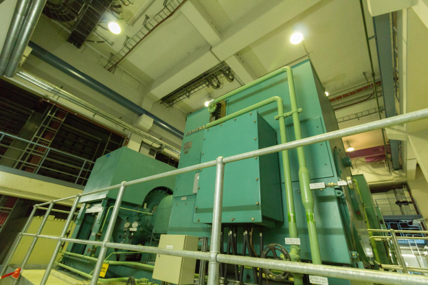 Großer industrieller Wärmetauscher in einem Gebäude, umgeben von Geländern, Rohren, Ventilen und Beleuchtungsequipment.