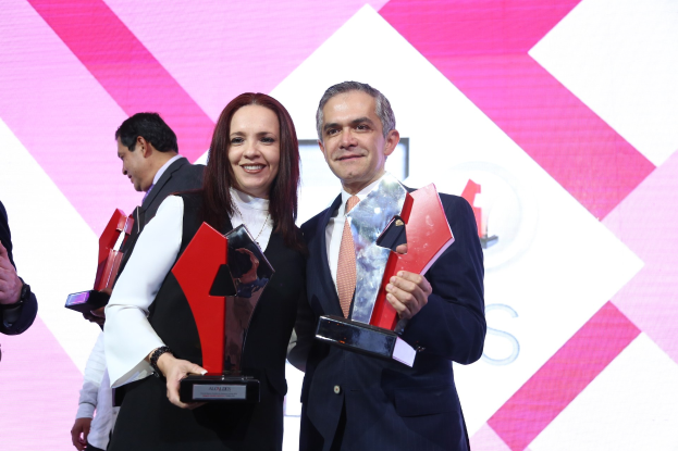 Zwei Personen auf einer Bühne mit Trophäen in den Händen, die strahlen, mit einem Awards-Ceremony-Hintergrund.