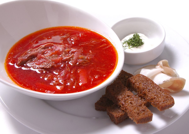 Weißer Teller mit einer Schüssel dicker roter Gazpacho-Suppe, leicht getoastetes Brot und Petersilie als Garnitur.