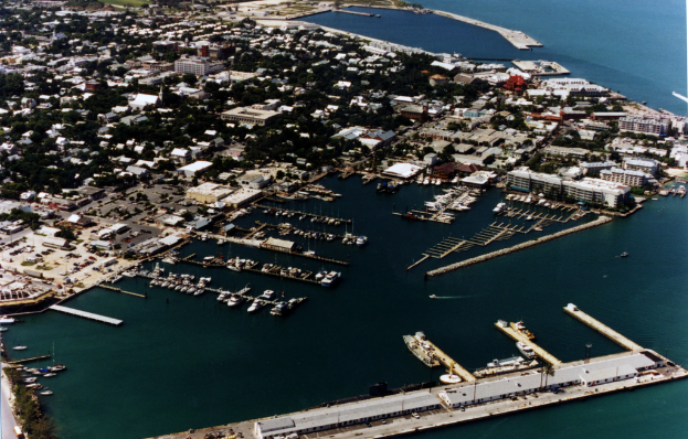 Eine Vogelperspektive einer Stadt mit zahlreichen Gebäuden, Meerwasser und einem Hafen unten vorne, mit mehreren Schiffen.
