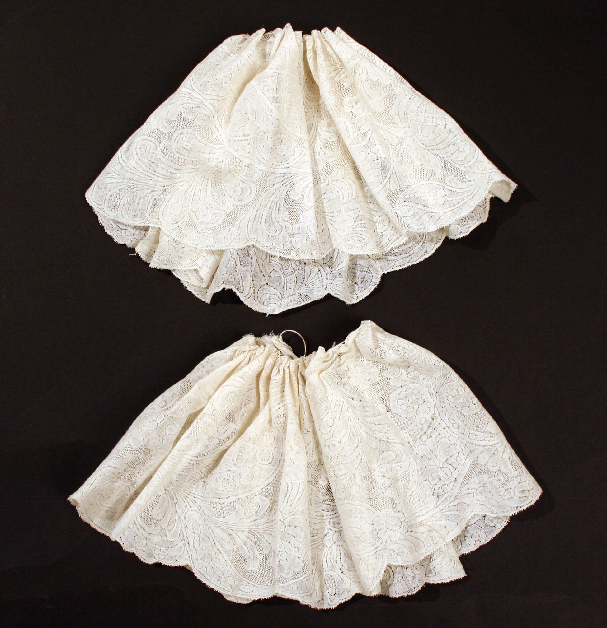 Zwei weiße Spitzeminiröcke mit zarten Mustern vor schwarzem Hintergrund.