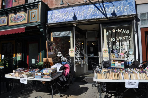 Bücher und Papiere auf Tischen, Stühle, Geschäfte, Bretter, Lampen und andere Gegenstände in einem Raum.
