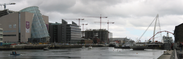 Ein Fluss mit Schiffen, eine Brücke, Gebäude, Kräne und der Himmel im Hintergrund.