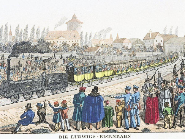 Eine Gruppe von Menschen, die um einen Zug auf einem Gleis herumstehen, wobei einige im Zug sitzen und andere auf dem Boden, in der Nähe eines Bahnhofs namens "Ludwigs-Eisenbahn, der erste Bahnhof in Deutschland", mit Gebäuden und Bäumen im Hintergrund.