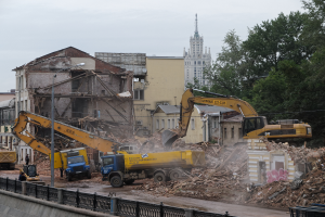 Eine belebte Abrissszene in Kiew, Ukraine, mit Kränen, Fahrzeugen, Menschen, Pfählen, Lampen, Schildern, Geländern und Bäumen, mit sichtbarem Himmel und einem Wasserzeichen auf dem Bild.