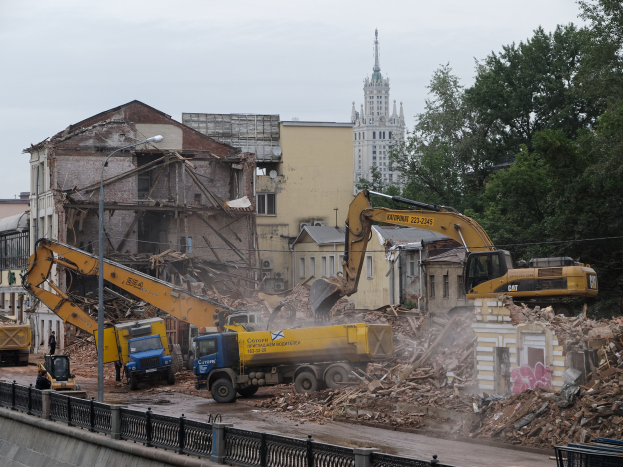 Eine belebte Abrissszene in Kiew, Ukraine, mit Kränen, Fahrzeugen, Menschen, Pfählen, Lampen, Schildern, Geländern und Bäumen, mit sichtbarem Himmel und einem Wasserzeichen auf dem Bild.