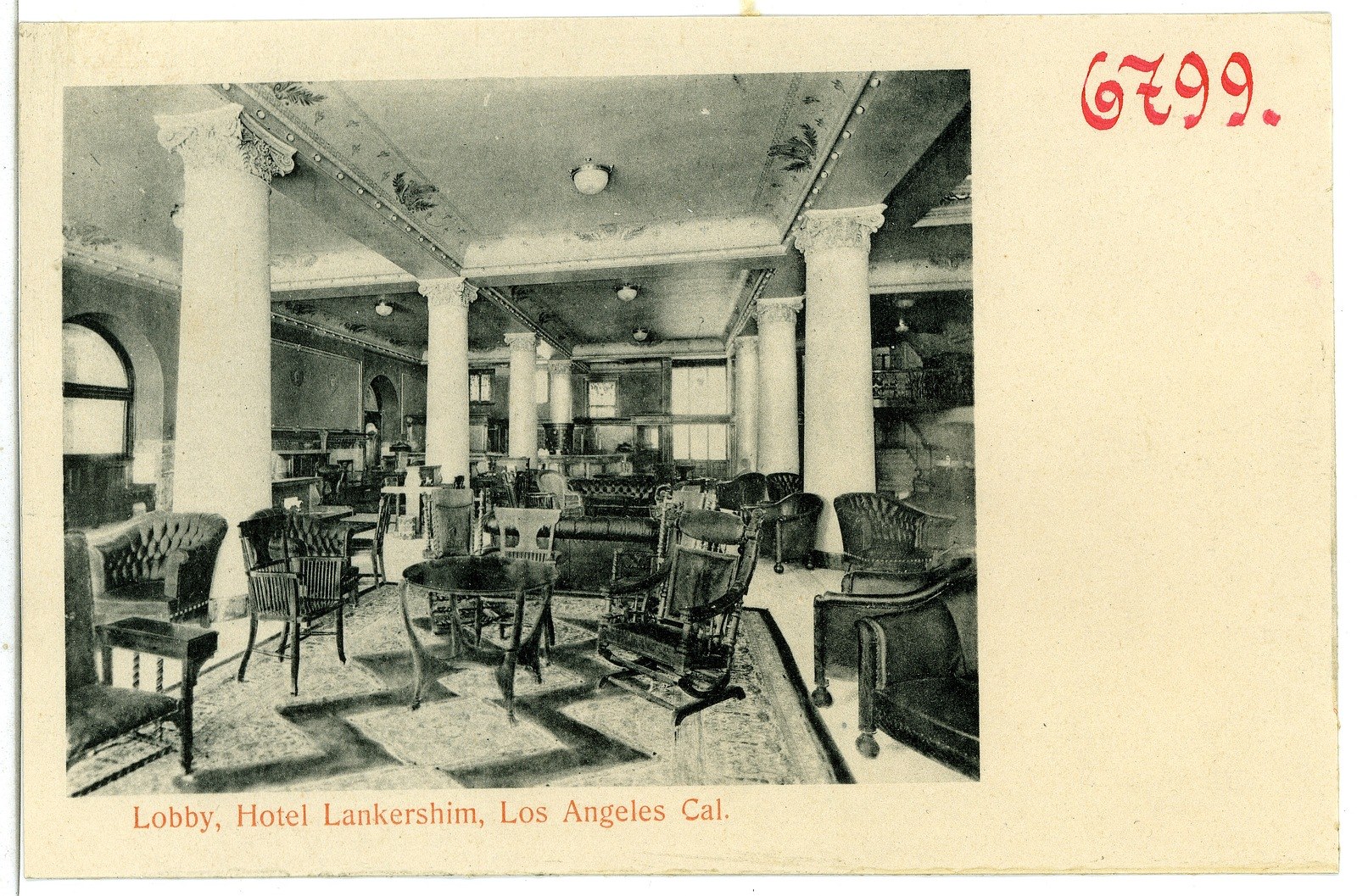 Black and white photo of a hotel lobby in Los Angeles with chairs, tables, pillars, ceiling lights, and windows on the left.