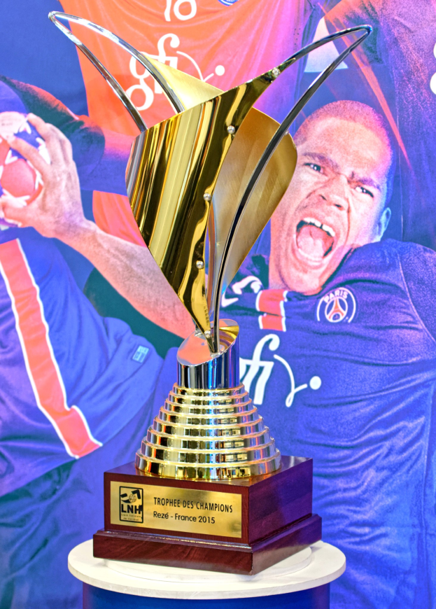 Ein silberner Pokal auf einem Tisch mit einem unscharfen Banner im Hintergrund, das ein Personenbild zeigt.