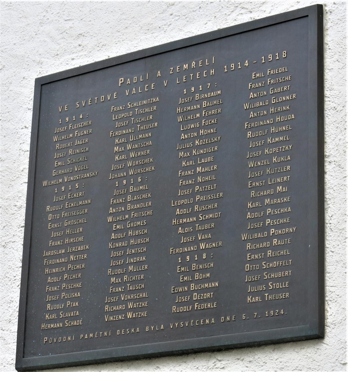 A stone plaque with inscribed text, likely a Holocaust memorial, mounted on a stone wall with plants at its base.