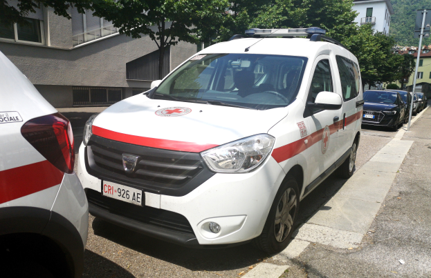 Zwei Ambulanzen nebeneinander auf einer Straße geparkt, mit Gebäuden, Bäumen und Masten im Hintergrund unter einem klaren blauen Himmel.