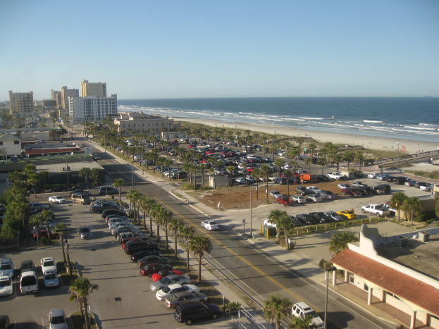 Fahrzeuge sind in der Nähe von Bäumen, Gebäuden und einem Ozean geparkt.