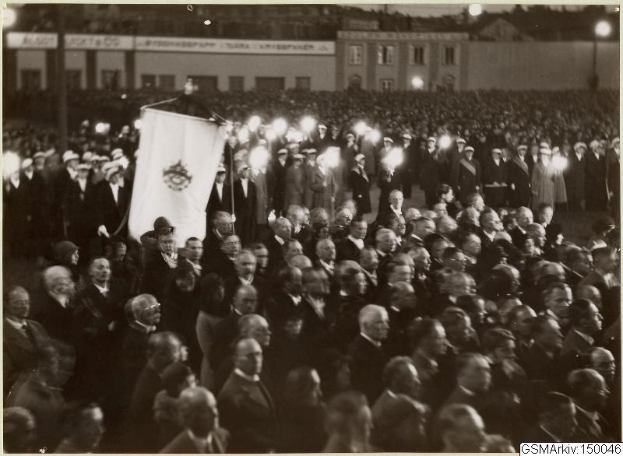 Schwarzes und weißes Foto einer großen Menge vor einem Gebäude, mit einer Person, die eine Fahne hält, Polen und Lichter im Hintergrund und Text unten, der 'Gustav Klimts Rede an der Berliner Mauer' lautet.