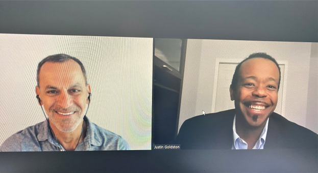 Zwei Männer bei einem Videoanruf, beide lächeln und tragen Headsets, in ein Gespräch vertieft.