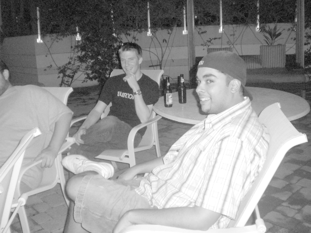 Drei Personen sitzen auf StÃ¼hlen, lÃ¤cheln und haben Weinflaschen auf einem Tisch hinter sich.