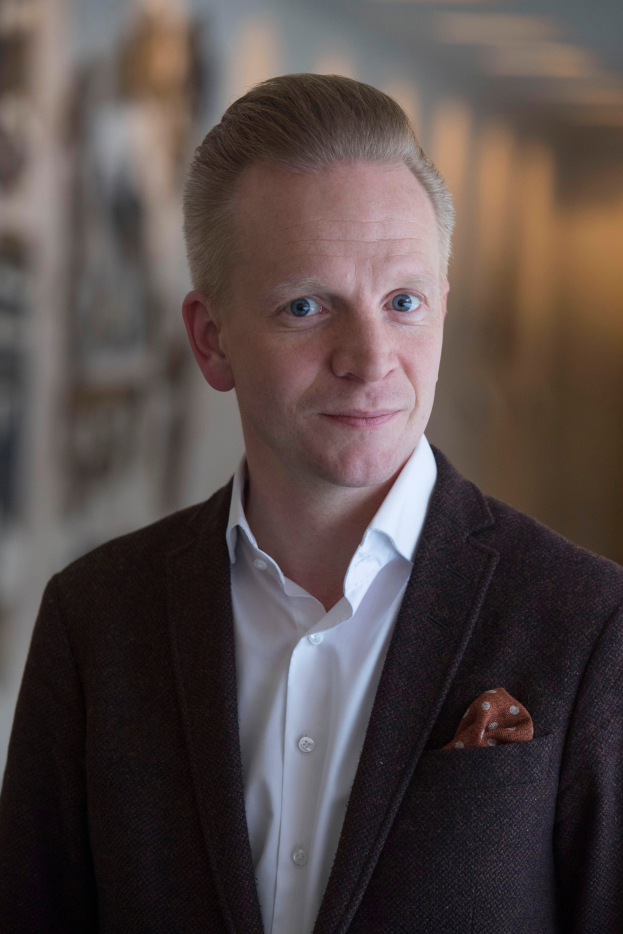 Ein Mann im Anzug und Krawatte steht vor einer Wand und schaut in die Ferne mit einem unscharfen Hintergrund.