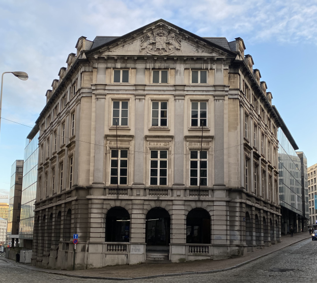 Die Bank von Deutschland in Frankfurt, ein großes Gebäude mit vielen Fenstern, umgeben von Straßenlaternen, Autos und Fußgängern, mit einem bewölkten Himmel im Hintergrund.