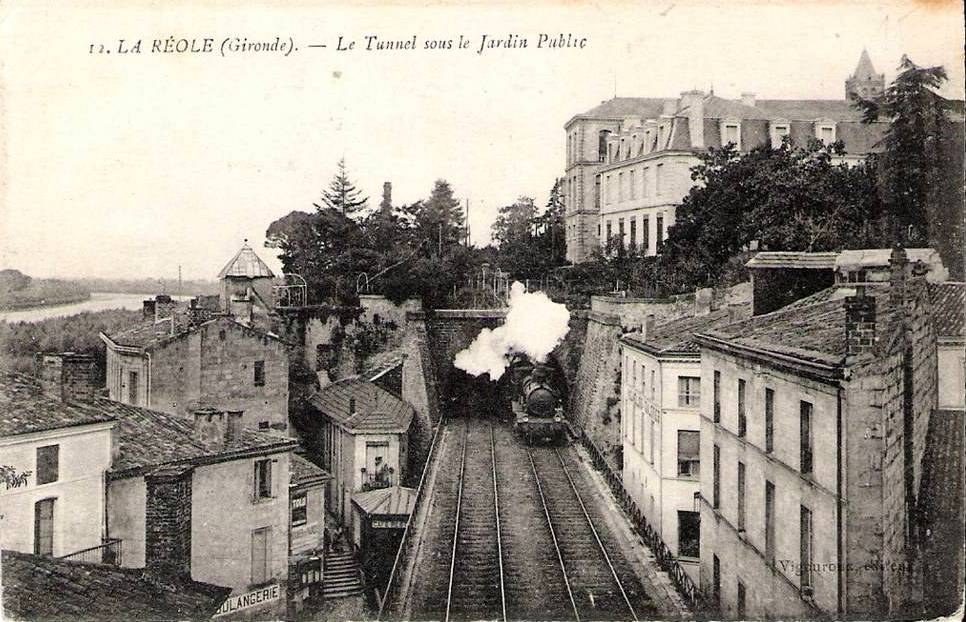 Black and white photo of a train on tracks with buildings, trees, and water, labeled "la réole gironde - le tunnel sous le jardin public" at the top.