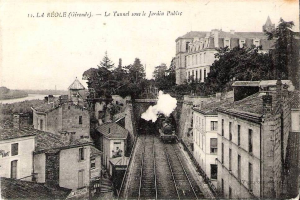 Black and white photo of a train on tracks with buildings, trees, and water, labeled "la réole gironde - le tunnel sous le jardin public" at the top.