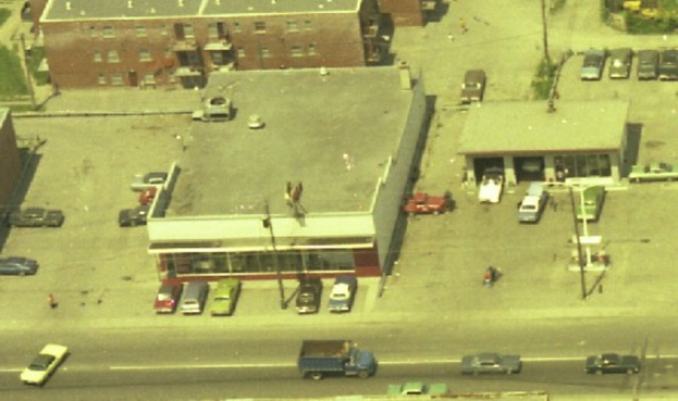 Eine Luftaufnahme einer Stadt mit zahlreichen Autos um Gebäude herum geparkt und einige Autos auf den Straßen fahrend.