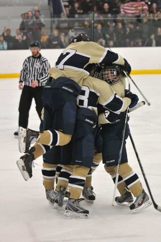 Hockeyspieler in Uniform und Helmen versammeln sich auf dem Eis während eines Spiels, mit Zuschauern im Hintergrund und einer Wand dahinter.