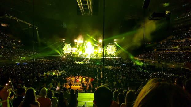 Große Menschenmenge in einem Stadion bei einem Konzert auf einer hell erleuchteten Bühne vor dunklem Hintergrund.