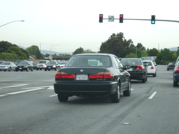 Eine vielbefahrene Straße mit mehreren Fahrzeugen, drei Strommasten und einer Ampel auf der rechten Seite unter einem klaren Himmel.
