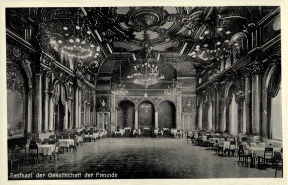 Black and white photo of a large room with tables, chairs, pillars, arches, and ceiling chandeliers, labeled "Festival der Gesellschaft der Freunde, Berlin" at the bottom.