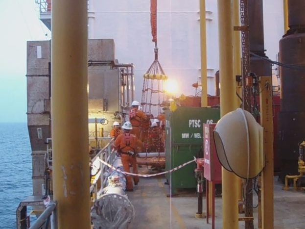 Ein Schiff mit Masten, Kisten und Geländern, das Menschen mit Helmen zeigt, vor Wasser.