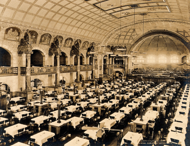 A vintage photograph of a large, ornate room with numerous tables and chairs, decorative pillars, wall-mounted sculptures, and ceiling lights.