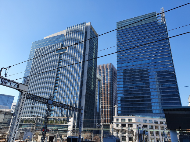 Eine Stadtstraße mit hohen Gebäuden, Strommasten, Kabeln, Straßenlaternen, Verkehrsampeln, Namensschildern, Bäumen und einem klaren blauen Himmel.