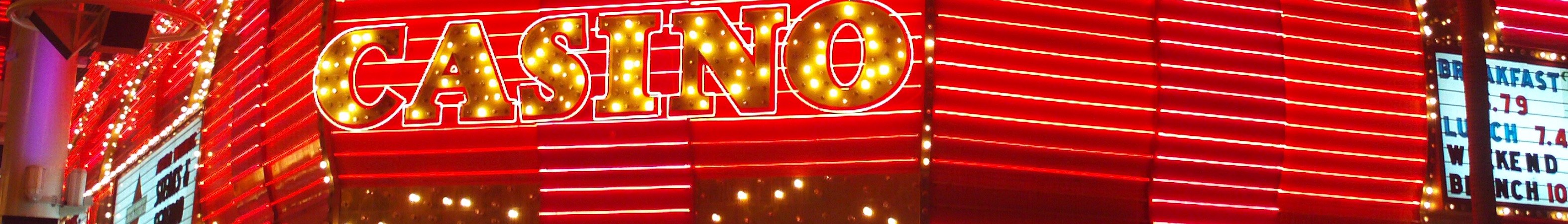 Casino-Schild bei Nacht vor einem Gebäude mit beleuchteter Wandtext und Werbetafeln, die die besten Casinos in Las Vegas auflisten.